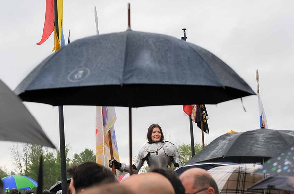 La jeune fille qui figure Jeanne d’Arc, portant un étendard, avec un parapluie visible au premier plan, lors des Fêtes de Jeanne d'Arc 2024 à Orléans
