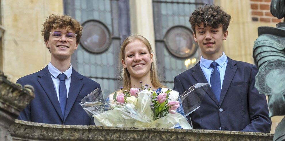 Sur un balcon en pierre, Clémence Miot, souriante et tenant un bouquet de fleurs, est entourée de Martin Paillat et d’Alexis Horstmann, tous trois habillés de manière élégante. Ils posent devant un bâtiment historique à l’occasion de la présentation de celle qui figurera la libératrice d’Orléans lors des prochaines fêtes.